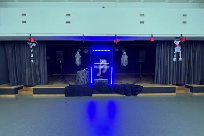 Scène décorée pour Halloween avec des lumières bleues, des squelettes suspendus et du matériel audio installé.