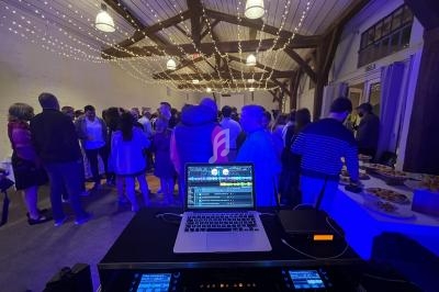 Vue d'une soirée festive avec des invités discutant sous des guirlandes lumineuses, depuis une table de DJ équipée.