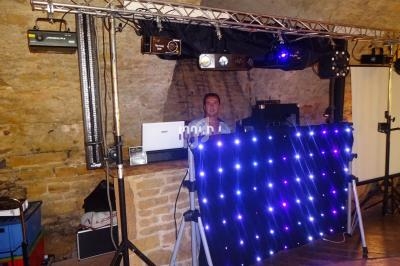 Un DJ derrière une table équipée de matériel audio et d'un panneau lumineux dans une salle en pierre.
