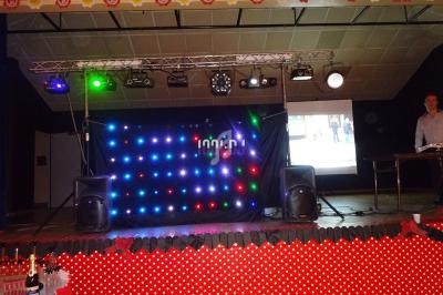 Scène décorée avec des lumières LED colorées, deux enceintes et un écran projetant une image en arrière-plan.