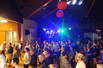 Personnes dansant en groupe dans une salle éclairée par des lumières colorées, décorée de lanternes rouges.