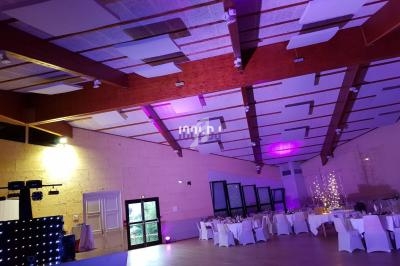 Salle de réception avec tables dressées, éclairage violet et plafond en bois avec panneaux acoustiques.