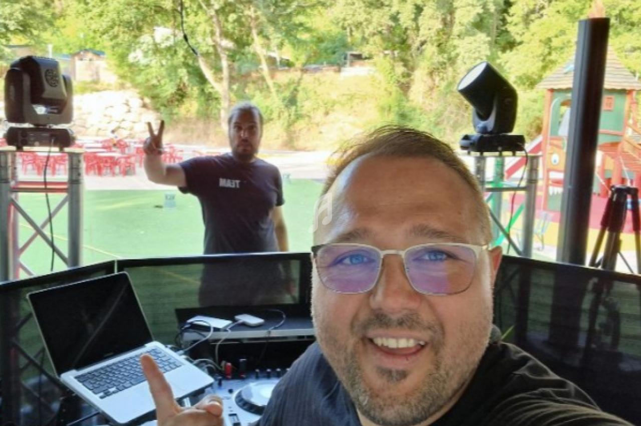 Deux hommes près d'une table de mixage en plein air, avec un parc verdoyant et des structures de jeux en arrière-plan.