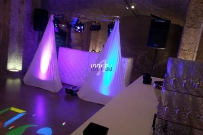 Installation de DJ avec éclairage coloré dans une salle en pierre, table de mixage et verres disposés au premier plan.