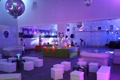 Salle décorée pour un événement, avec éclairage coloré, canapés blancs, tables basses et ambiance festive.