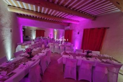 Salle de réception décorée avec des tables dressées, nappes blanches et éclairage d'ambiance rose.
