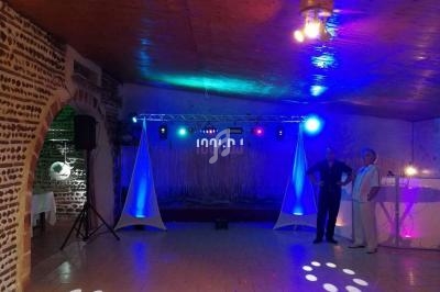 Salle de réception avec éclairage coloré, piste de danse vide et deux personnes debout près d'une table lumineuse.