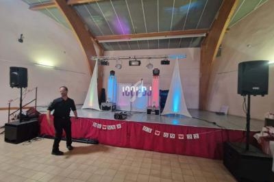 Scène décorée avec éclairages colorés, équipement de DJ et haut-parleurs dans une salle avec plafond en bois.