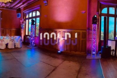 Salle de réception décorée avec des tables rondes, nappes blanches, serviettes roses et éclairage coloré.