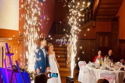 Un couple en tenue de mariage pose près de fontaines d'étincelles dans une salle décorée avec des invités assis.