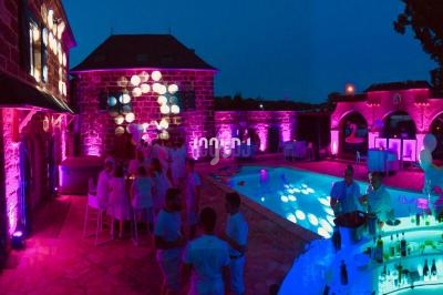 Soirée en extérieur avec éclairages colorés, piscine illuminée et invités en tenue blanche.