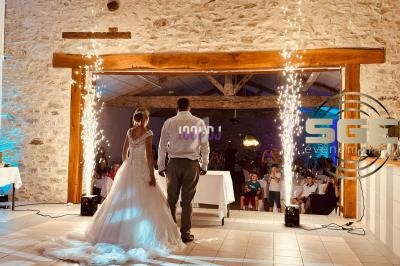 Un couple de mariés entre dans une salle de réception en pierre, entouré de jets d'étincelles festives.