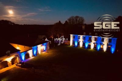 Vue nocturne d'un bâtiment éclairé par des lumières bleues et blanches, avec un logo ’SGE événementiel’ superposé.