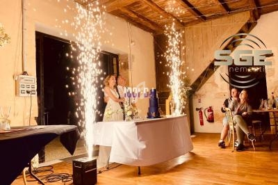 Un couple se tient derrière une table lors d'une fête, entouré d'étincelles dans une salle en bois.