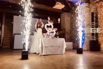 Mariée levant les bras devant une pièce montée éclairée par des fontaines d'étincelles dans une salle en pierre.