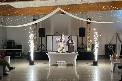 Un couple assis à une table décorée, entouré de fontaines lumineuses dans une salle de réception éclairée.