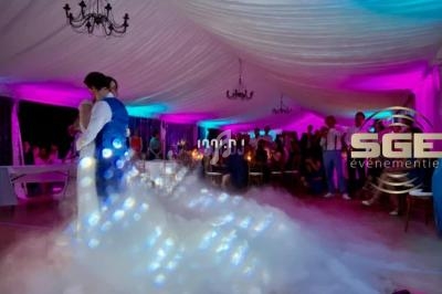 Un couple danse dans une salle éclairée de lumières colorées, avec un effet de fumée au sol.