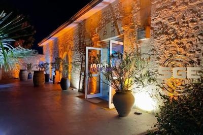 Façade en pierre éclairée de nuit avec des pots de plantes et une entrée vitrée illuminée.