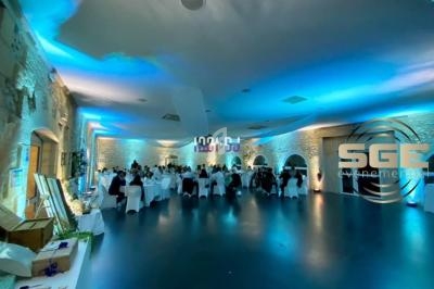 Salle de réception éclairée en bleu avec des invités assis à des tables rondes et des murs en pierre apparente.