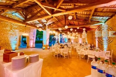 Salle de réception en pierre avec tables dressées, décorations lumineuses et lanternes suspendues au plafond en bois.