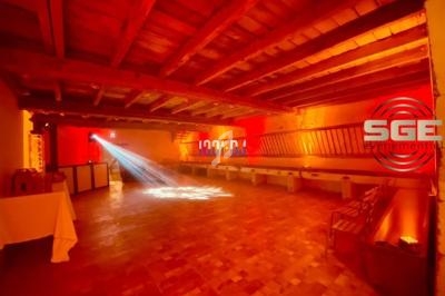 Salle en bois avec éclairage rouge et orange, projecteur lumineux au sol et logo ’SGE événementiel’ sur le mur.