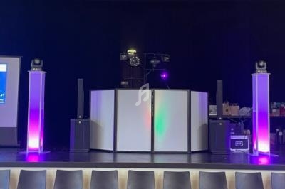 Installation de matériel de sonorisation et d'éclairage sur une scène, avec des colonnes lumineuses et un écran à gauche.