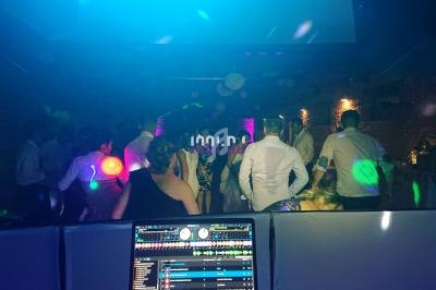 Des personnes dansent sous des jeux de lumière colorés dans une salle sombre, vue depuis une table de mixage.