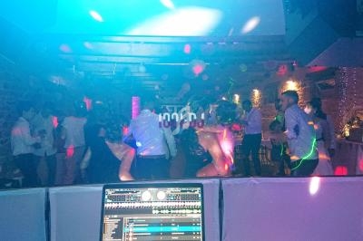 Des personnes dansent dans une salle éclairée par des lumières colorées, vue depuis une table de mixage.