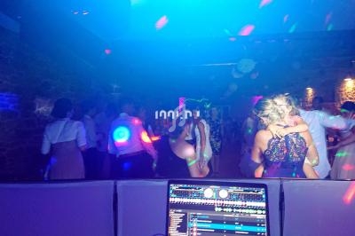 Des personnes dansent dans une salle sombre éclairée par des lumières colorées, avec une table de mixage au premier plan.