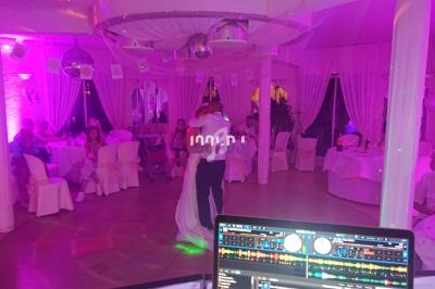 Un couple danse au centre d'une salle éclairée de lumières roses, entouré d'invités assis à des tables décorées.