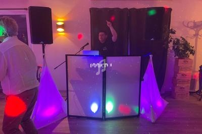 Un DJ anime une soirée avec des lumières colorées, un homme danse au premier plan.
