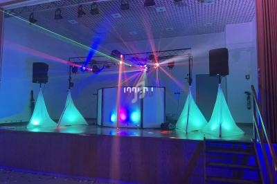 Scène de soirée avec éclairage coloré, lasers, enceintes et structure de DJ installée sur une estrade.