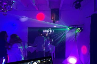Vue d'une soirée dansante avec des jeux de lumière colorés, un DJ et un ordinateur affichant une interface musicale.