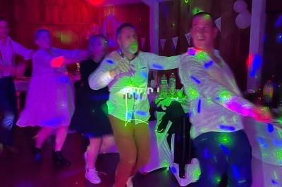 Des personnes dansent dans une salle éclairée par des lumières colorées, décorée pour une fête.