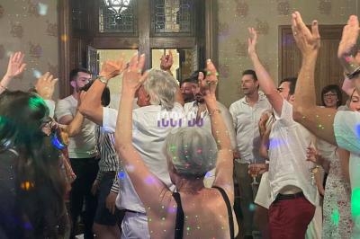 Groupe de personnes dansant dans une pièce éclairée par des lumières colorées, ambiance festive et conviviale.