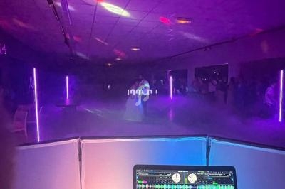 Un couple danse dans une salle sombre éclairée par des lumières colorées, vue depuis une table de mixage.