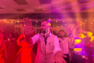 Un homme en gilet clair danse au milieu d'une foule sous des lumières colorées dans une ambiance festive.