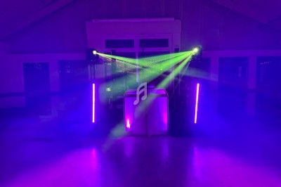 Jeux de lumières violettes et vertes éclairant une scène avec un équipement audio dans une salle sombre.