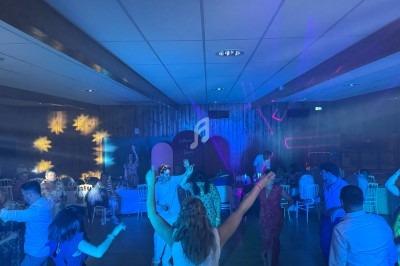 Des personnes dansent sous des lumières colorées dans une salle avec un décor en bois et des tables en arrière-plan.