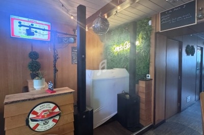 Intérieur d'un café avec décoration végétale, guirlandes lumineuses, écran mural et mobilier en bois.