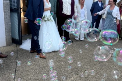 Un couple de mariés pose avec des invités devant un bâtiment, entourés de bulles de savon.