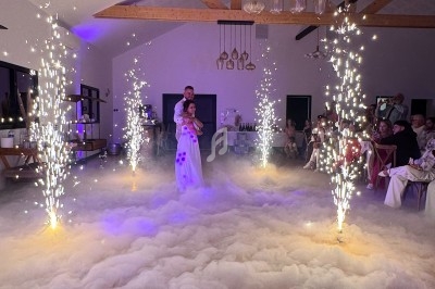 Un couple danse au centre d'une salle éclairée, entouré de fumée au sol et de jets d'étincelles.