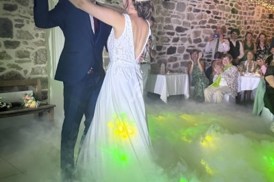 Un couple danse dans une salle en pierre, entouré de fumée et de lumières colorées, sous le regard des invités.