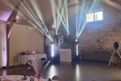 Salle de réception décorée avec des tables dressées, des faisceaux lumineux et un mur en pierre apparente.