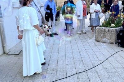 Un couple en tenue de mariage se tient devant un groupe de personnes sur une place pavée, entouré de bulles de savon.