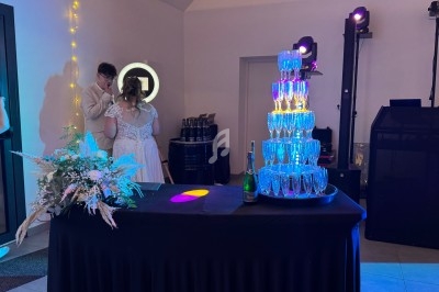Tour de flûtes à champagne illuminées sur une table noire, décorée de fleurs, dans une salle de réception.