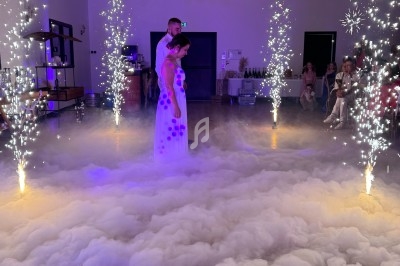 Un couple danse au milieu d'une salle éclairée, entouré de fumée au sol et de jets d'étincelles.