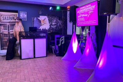Salle de karaoké avec éclairage coloré, décorations sur le thème du Far West et panneau d'information lumineux.