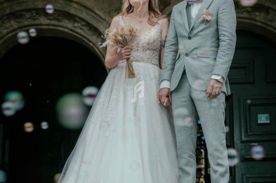 Un couple en tenue de mariage se tient sur les marches d'un bâtiment ancien, entouré de bulles de savon.