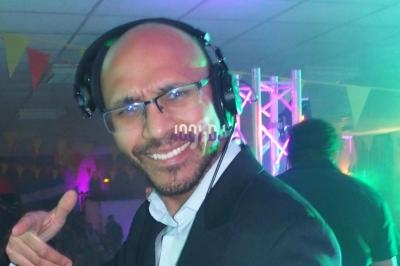 Homme souriant portant un casque audio dans une ambiance festive avec éclairages colorés et guirlandes en arrière-plan.
